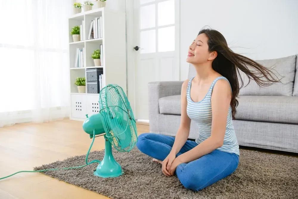 a person sitting on the floor with her eyes closed and a fan in the background