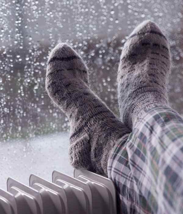 feet wearing gray woolen socks, warming cold feet on oil heater in the rainfall winter season