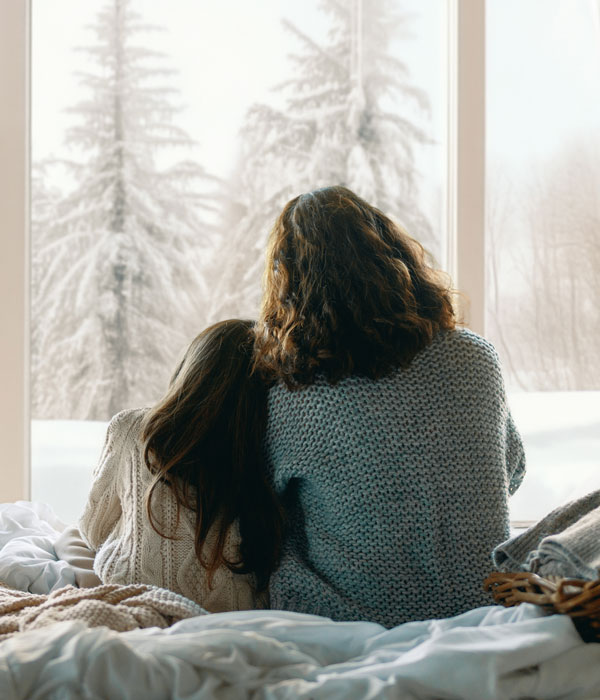 Mother and daughter enjoying winter nature from the window inside home